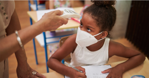 LFTM-featuredimage - Mississippi First Teacher checks student's temperature with a forehead thermometer while student wears a mask at school.
