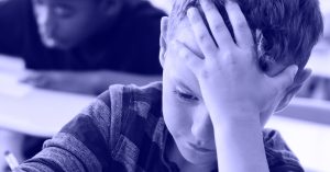 Elementary students taking a test in classroom - Mississippi First Young student in a classroom rests his head on his hand, looking tired or stressed.